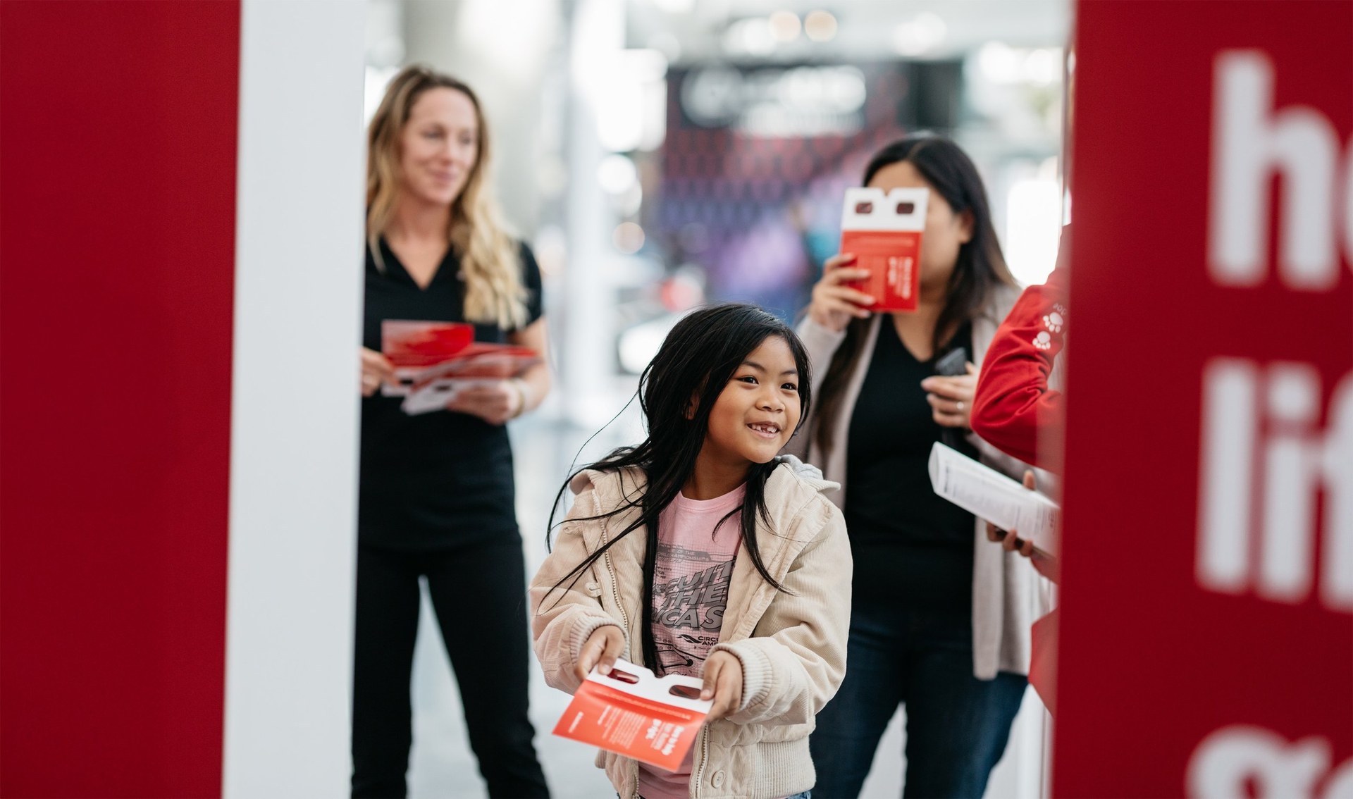 A girl grinning, holding out a red cardboard viewer at the dealership
