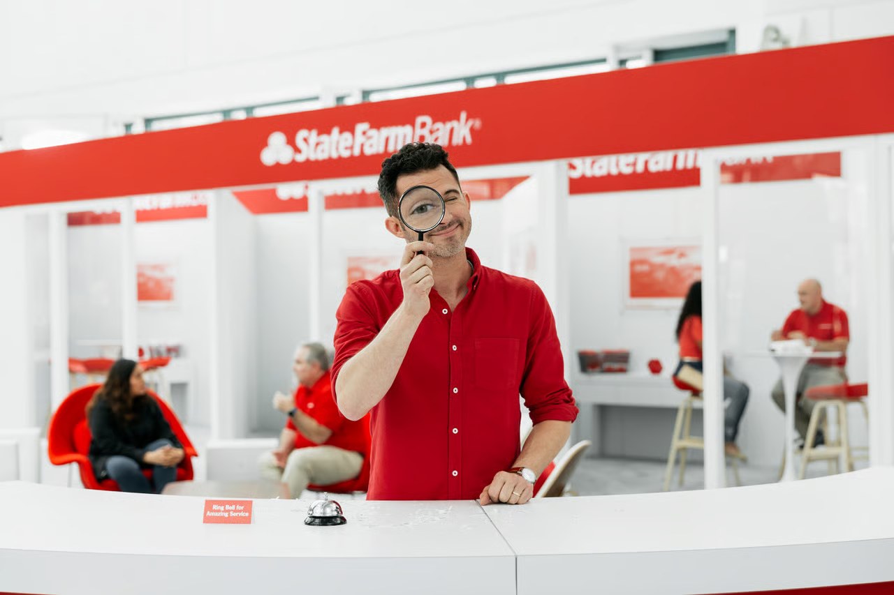 Justin Willman at the reception desk, looking through a magnifying glass