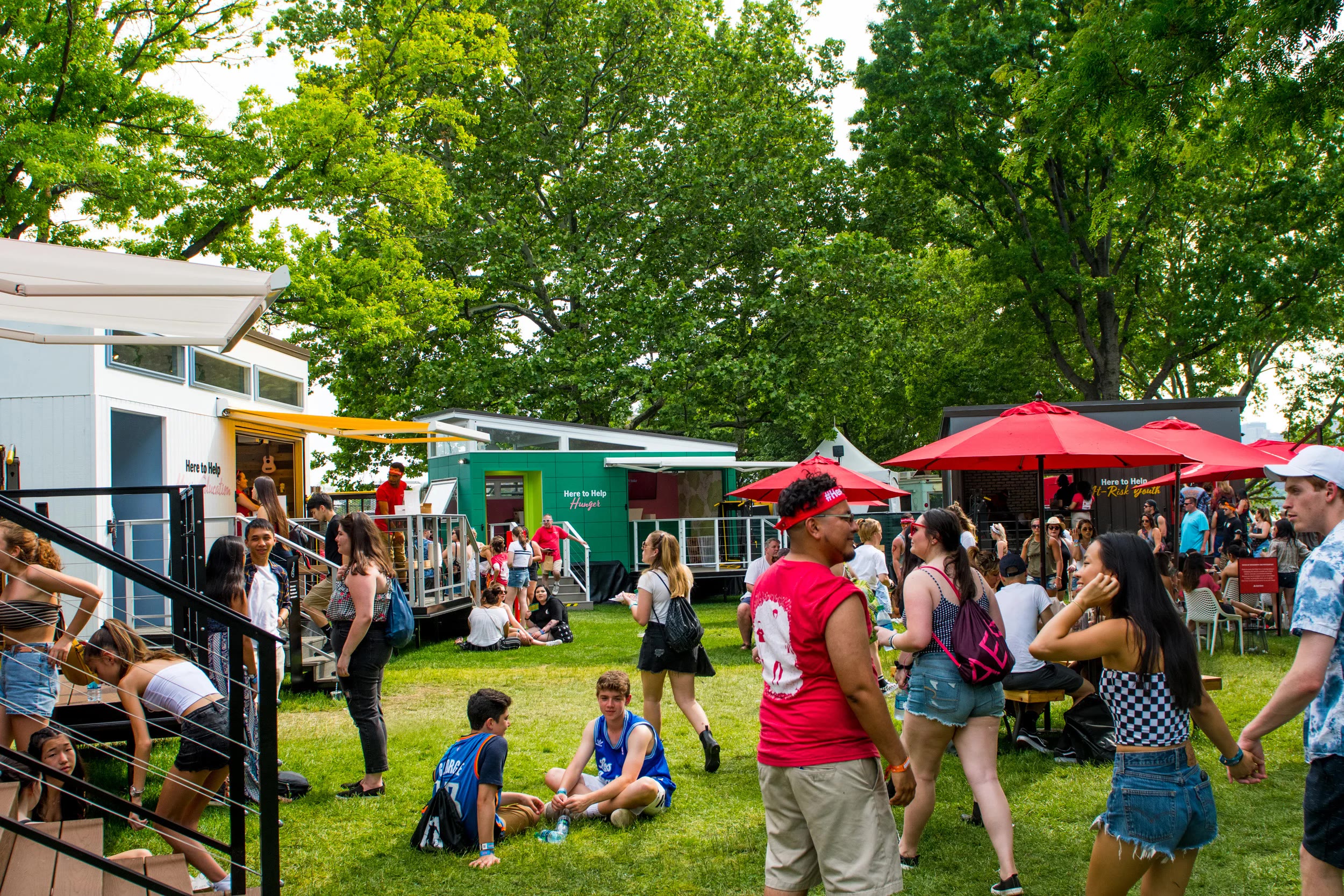 The Neighborhood of Good block at a festival: cabins, red umbrellas and the crowd